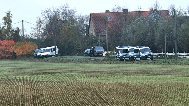 Neblige Herbst-Stimmung auf dem Land, Polizeiautos stehen am Rande eines Ackers, im Hintergrund ist ein Haus mit Zaun umgeben von Bäumen zu sehen