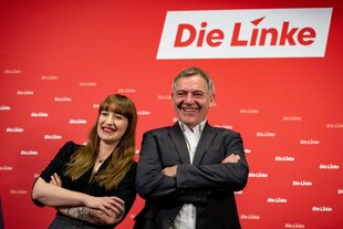 Heidi Reichinnek und Jan van Aken stehen mit verschränkten Armen vor dem Logo ihrer Partei