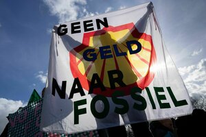 Ein Mensch steht hinter einem Plakat mit Shell Logo und der holländischen Aufschrift: Kein Geld für Fossil