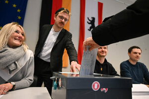 Das Bild zeigt eine Hand, die einen Wahlzettel in eine Wahlurne steckt.