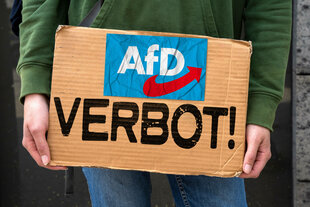 Eine Person hält ein Schild mit der Aufschrift: "AFD Verbot!"