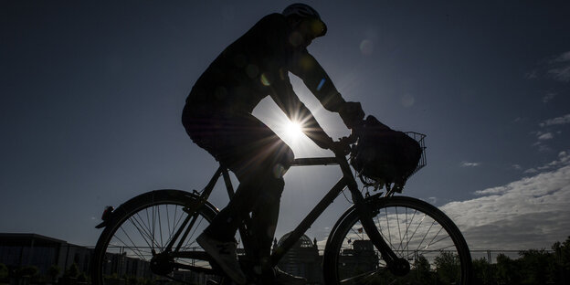 Mensch auf Fahrrad. Im Hintergrund die Morgnsonne.