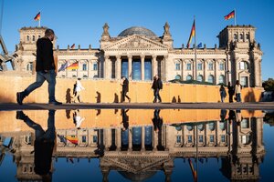 Menschen an einem sonnigen Herbsttag am Reichstag, dessen Westfassade sich in einer grossen Pfuetze spiegelt