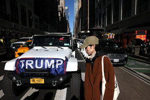 Ein Fußgänger überquert die Straße vor einem Trump-Anhänger in der Nähe des Madison Square Garden - er trägt ein MAGA Basecap - den Kühler seines überdimensionierten Monstertrucks hat er mit einem "Trump" Banner geschmückt