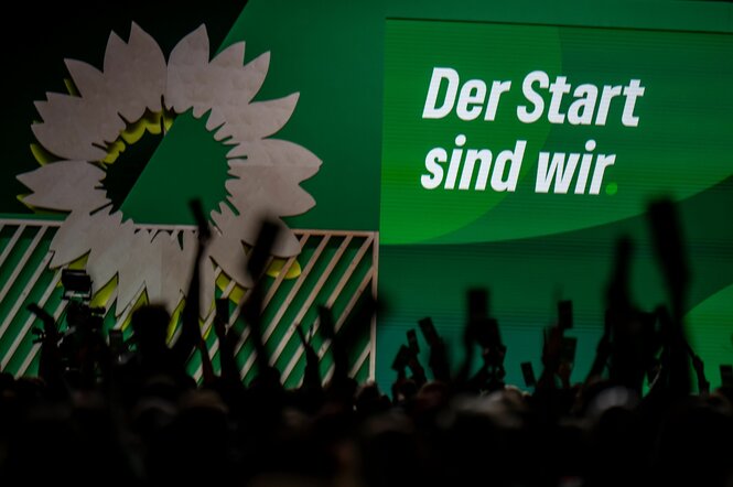 Hände mit Abstimmungskarten vor der Parteitagsbühne