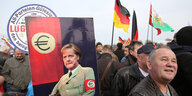 Pegida-Demo mit Deutschlandfahnen, einem Plakat von Merkel im Hitler-Look ein älterer Mann grinst glückselig
