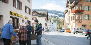 SchweizerInnen geben in einer hölzernen Wahlurne auf offener Straße ihre Stimme ab. Im Hintergrund Berge