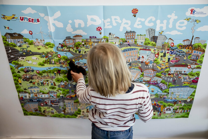 Ein Kind steht mit dem Rücken zur Kamera vor einem Plakat des Deutschen Kinderhilfswerks mit der Aufschrift «Kinderrechte»