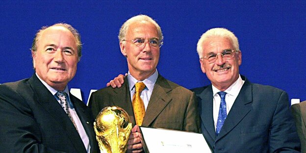 Blatter, Beckenbauer und Radmann freuen sich und halten den WM-Pokal