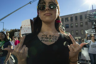 Eine Person zeigt bei einer Demonstration ihre Mittelfinger.