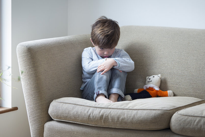 Ein kleiner Junge sitzt auf einem Sofa und schaut verängstigt