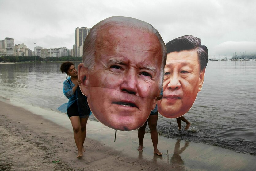 Aktivisten tragen große Köpfe aus Pappe von Joe Biden und Xi Jinping am Strand entlang