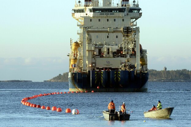 Ein großes Installationsschiff mit Aufbauten auf dem Meer, zwei kleine Boots befinden sich vor dem Schiff, eine Markierungsleine mit roten Bojen zieht das Schiff hinter sich her