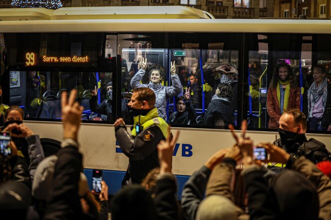 Demonstranten mit Palästinensertüchern gestikulieren in einem Bus, davor Polizisten