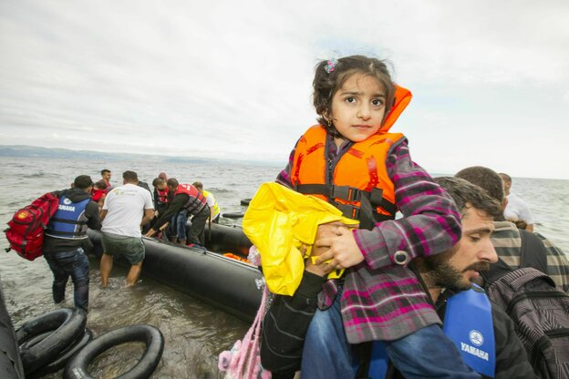 Ankommende Geföüchtete aus Syrien mit dem Schlauchboot, ein Kind in Rettungsweste wird von einem Helfer getragen