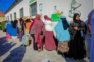 Frauen in traditioneller bunter Kleidung und Kopftüchern stehen Schlange vor einem Wahllokal in der Hitze