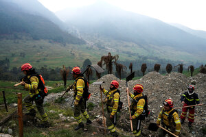 Feuerwehrleute in gelben Uniformen und roten Helmen auf dem Kopf stehen Schlange, sie sind auf dem Weg zum löschen, im Hintergrund bewaldete Höhenzüge