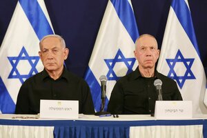 Benjamin Netanjahu und Yoav Gallant sitzen mit ernsten Minen an einem Tisch während einer Pressekonferenz. Hinter ihnen sind Fahnen Israels drapiert