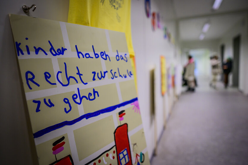 Ein Pappschild mit blauer Aufschrift lehnt an der Wand eines langen Flures