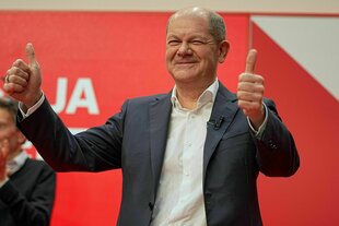 Bundeskanzler Olaf Scholz hält beide Daumen hoch und lacht