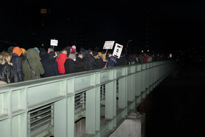 Viele Menschen bei einer Demonstration, die über eine Brücke in die Dunkelheit führt.