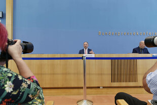 Marco Wanderwitz, klein im Bild, spricht auf dem Podium der Bundespressekonferenz