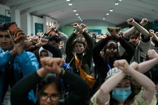 Aktivist*innen verschränken die Arme über dem Kopf bei einer Demonstration auf der UN-Klimakonferenz.