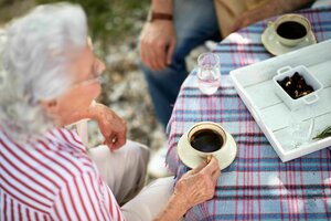 Eine ältere Dame sitzt an einem gedeckten Tisch und trinkt Kaffee