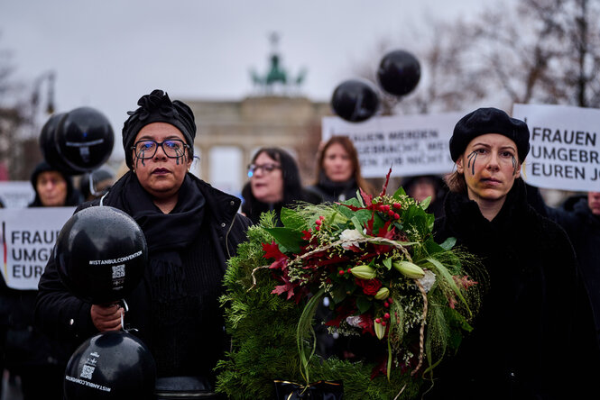 Zwei in Schwarz gekleidete Frauen tragen einen Trauerkranz