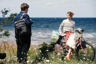 Eine Frau steht an ihrem Fahrrad und unterhält sich mit einem Mann, im Hintergrund das Meer.Szene aus Christian Petzolds Film "Roter Himmel"