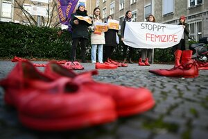 Rote Schuhe stehen auf dem Asphalt, eine Gruppe vn sechs Frauen hält ein Transparent mit der aufschrift: Stoppt Femizide