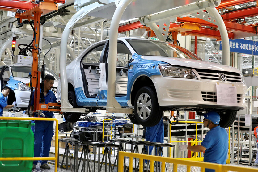 Werkshalle von VW , Arbeiter stehen am Band unter und neben der Karosserie eines Autos, an dem sie arbeiten