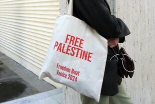 Eine Person mit einer Stofftasche mit dem Aufdruck "Free Palestine" steht an einer Wand