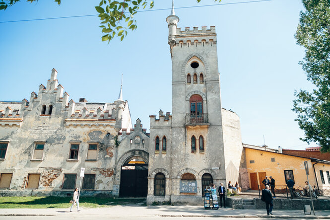 Die Fassade der unrenovierten Fabrik im neogotischen Ritterschloss-Stil in verwaschenem Weiß.