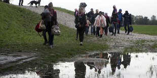 Mehrere Flüchtlinge gehen an einer großen Pfütze vorbei