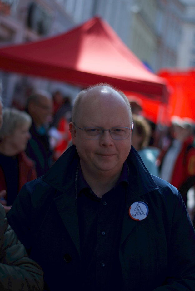 Zu sehen ist der Abgeordnete Stefan Seidler vom Südschleswigschen Wählerverband auf einer Straße während des Wahlkampfs. Sein Gesicht ist groß im Vordergrund, hinter ihm rote Gartenpavillons, die Parteistände vor Sonne und Regen schützen.