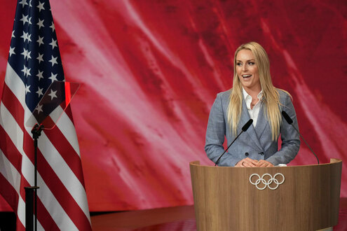 Lindsey Vonn steht an einem Rednerpult mit olympischen Ringen, an der Seite die US-Flagge