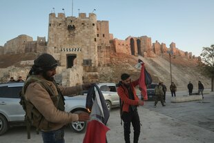 Zwei Männer zünden vor der Altstadtkulisse von Aleppo die Flaggen des syrischen Machthabers Assad an