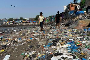 Menschen spazieren in Mumbai an der Küste des Arabischen Meeres an Plastikmüll vorbei.