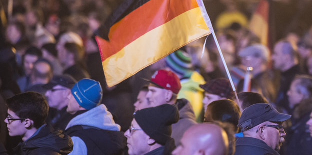 Pegida-Anhänger mit einer Deutschlandfahne in einer Menschenmenge.