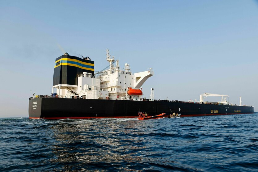 Zwei kleine Schlauchbooten fahren eng an einem rießogen Öltanker vorbei, der auf der Ostsee fährt