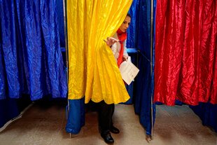 Eine Frau verlässt in Bukarest eine Wahlkabine, deren Vorhang die Farben der rumänischen Nationalflagge hat, bei den Parlamentswahlen in Rumänien am Sonntag, 1. Dezember 2024