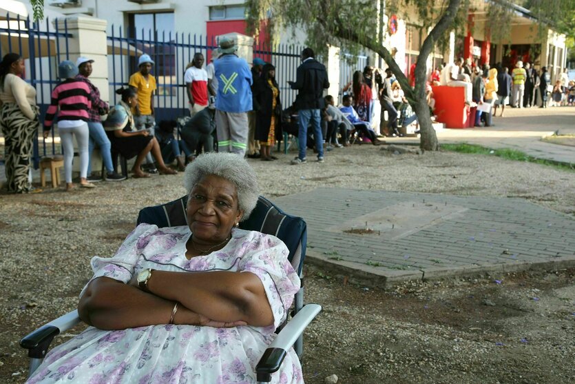 Eine Frau sitzt in einem Sessel, während Namibier in der Schlange stehen, um ihre Stimme bei der Präsidentschafts- und Parlamentswahlen abzugeben