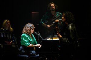 Eine Frau in grüner Bluse singt an einem Klavier. Im Vordergrund singt eine zweite Frau, im Hintergrund spielt eine Band