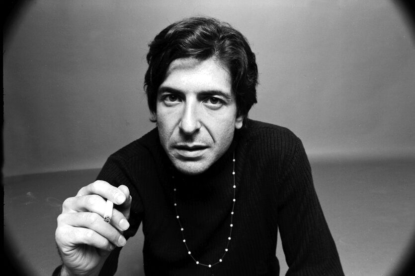 Leonard Cohen blickt in die Kamera, schwarz gekleidet und mit Zigarette in der Hand.