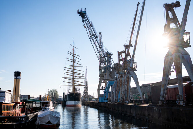 Alte Schiffe und Kräne in einem Hafen.