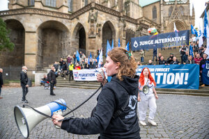 Eine Frau mit Megaphon vor einem Stand der Jungen Alternative