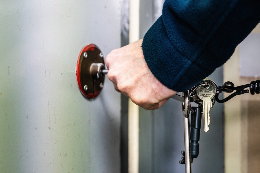 Eine Hand hält einen großen Schlüsselbund und dreht einen Schlüssel im Schloss einer schweren Tür