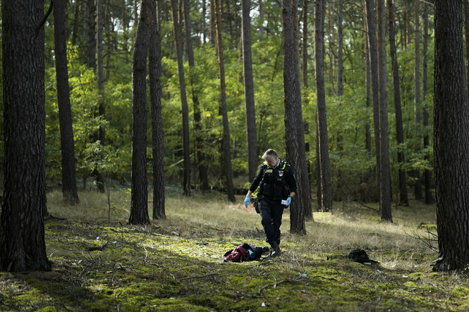 Ein Polizist schaut Kleidung an, die auf einem Waldboden liegt