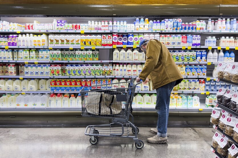 Ein Mann beugt sich zu Milchflaschen in einem Supermarktregal